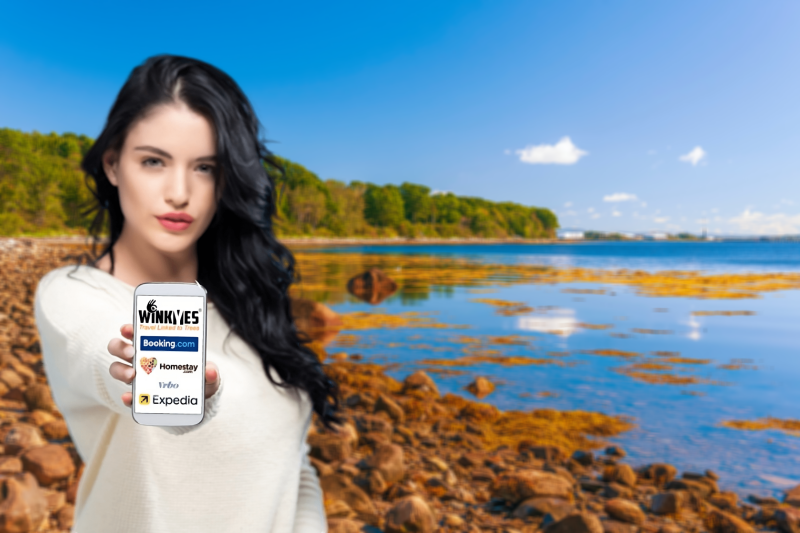 Girl on the Seashore Showing Smartphone Screen with WINKYES Travel Linked to Trees Web App. sustainable travel, green travel