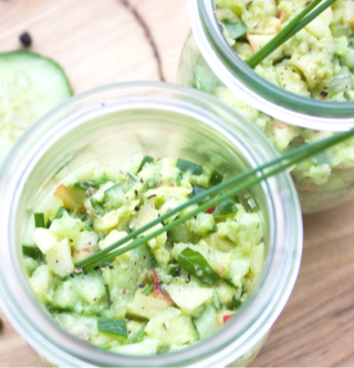 A vibrant, healthy salad of diced green apples, cucumbers, and avocados topped with fresh mint leaves in a glass bowl