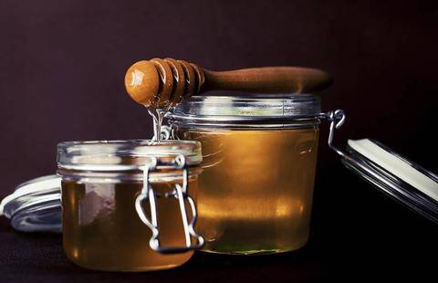 A glass jar of golden CBD-infused honey with a wooden honey dripper laying on 2 glass jars
