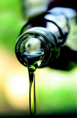 Green cannabis-enriched oil being strained through cheesecloth into a glass storage jar pouring from the mouth