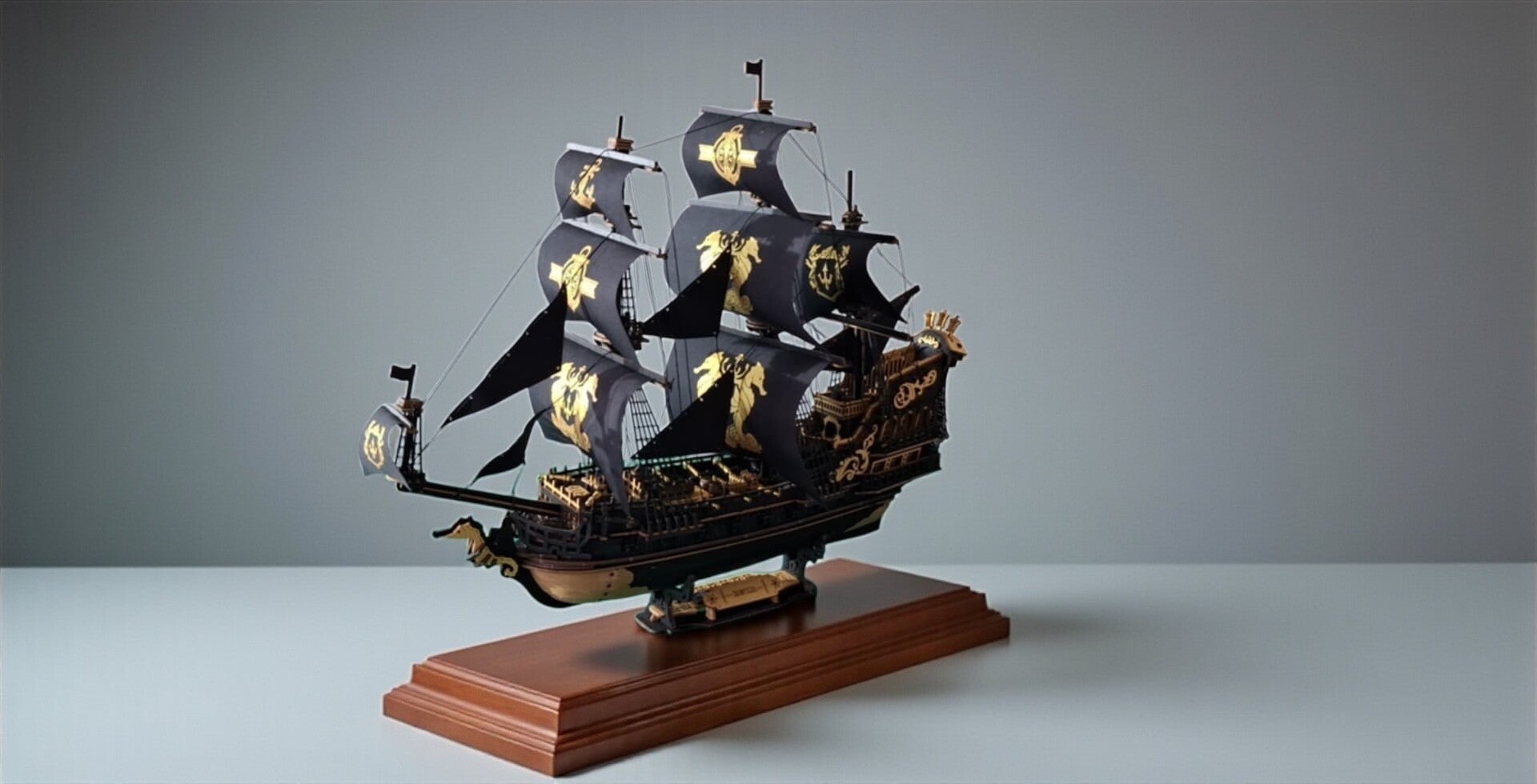 Gedetailleerd model van een piratenschip met zwarte zeilen en gouden schedel-emblemen, geplaatst op een houten sokkel. Het schip heeft meerdere masten, fijn tuigage en sierlijke ornamenten, en straalt vakmanschap en avontuur uit. Robotime MCB02