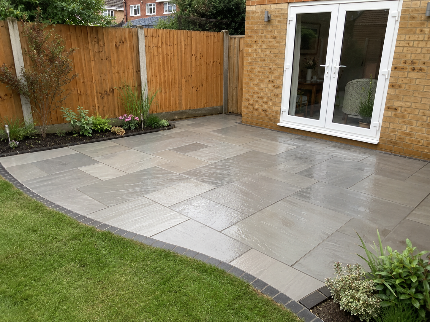 Completed grey paving patio installation with curved lawn edge