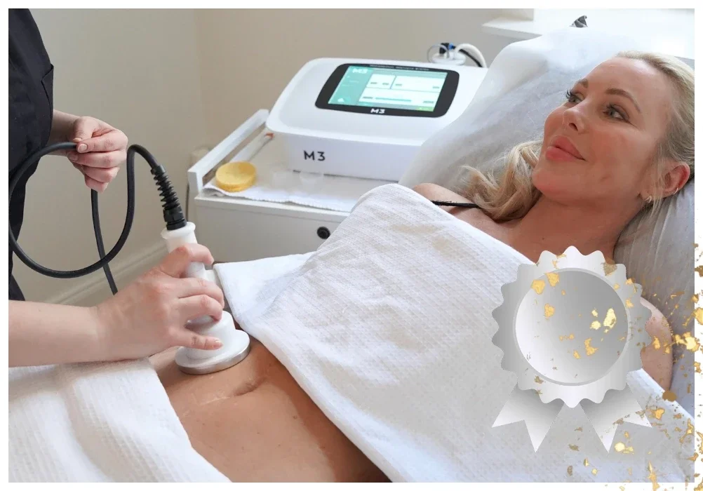 Nainen makaa hoitopedillä vartalonmuokkaushoidossa, jossa käytetään rasvanpoistolaitetta vatsan alueella. Kuvan oikeassa alalaidassa on hopeinen mitali, joka kuvastaa tuotepakettia.