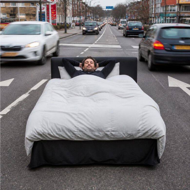 Man ligt ontspannen in bed tussen druk verkeer – waarom rust nemen soms moeilijker is dan hard werken