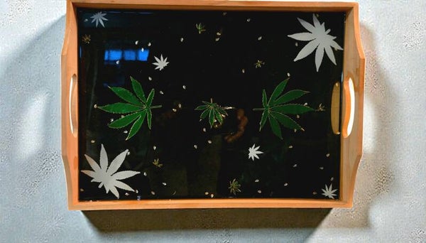 Decorative Resin Traycustom-made wooden rolling tray featuring a black background with cannabis leaf designs and glitter, likely sealed with epoxy resin. These trays are used as smoking accessories for rolling cigarettes or joints, with raised edges to pr