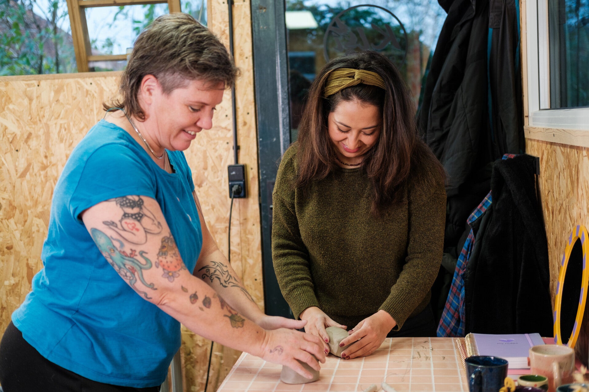 Twee personen zijn klei aan het kneden tijdens een pottenbak workshop met een lach op hun gezicht