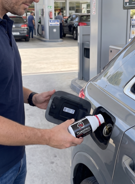 Hombre echando aditivo para diésel Tuakpro en el depósito de combustible de un coche en la gasolinera