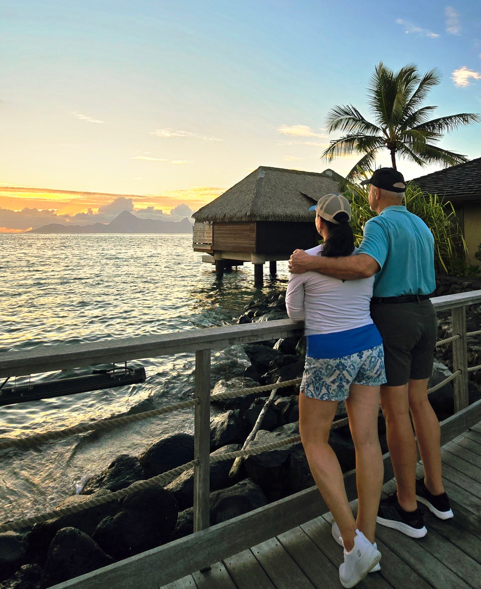Travel writer Terri Guthrie and her husband Ron watching a tropical sunset beside overwater bungalow resorts in Tahiti.