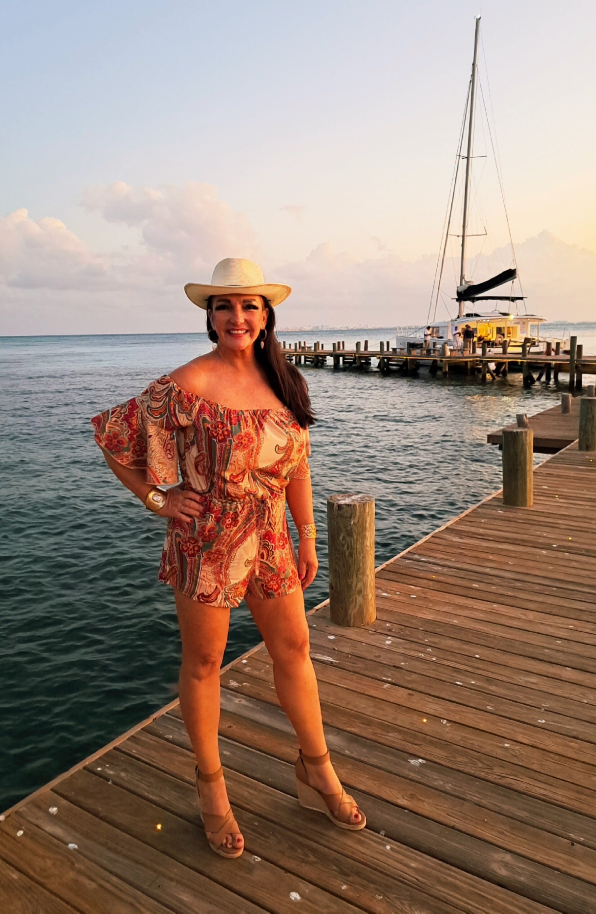 Travel journalist Terri Guthrie in a sundress standing on a dock at sunset with a luxury yacht behind her.