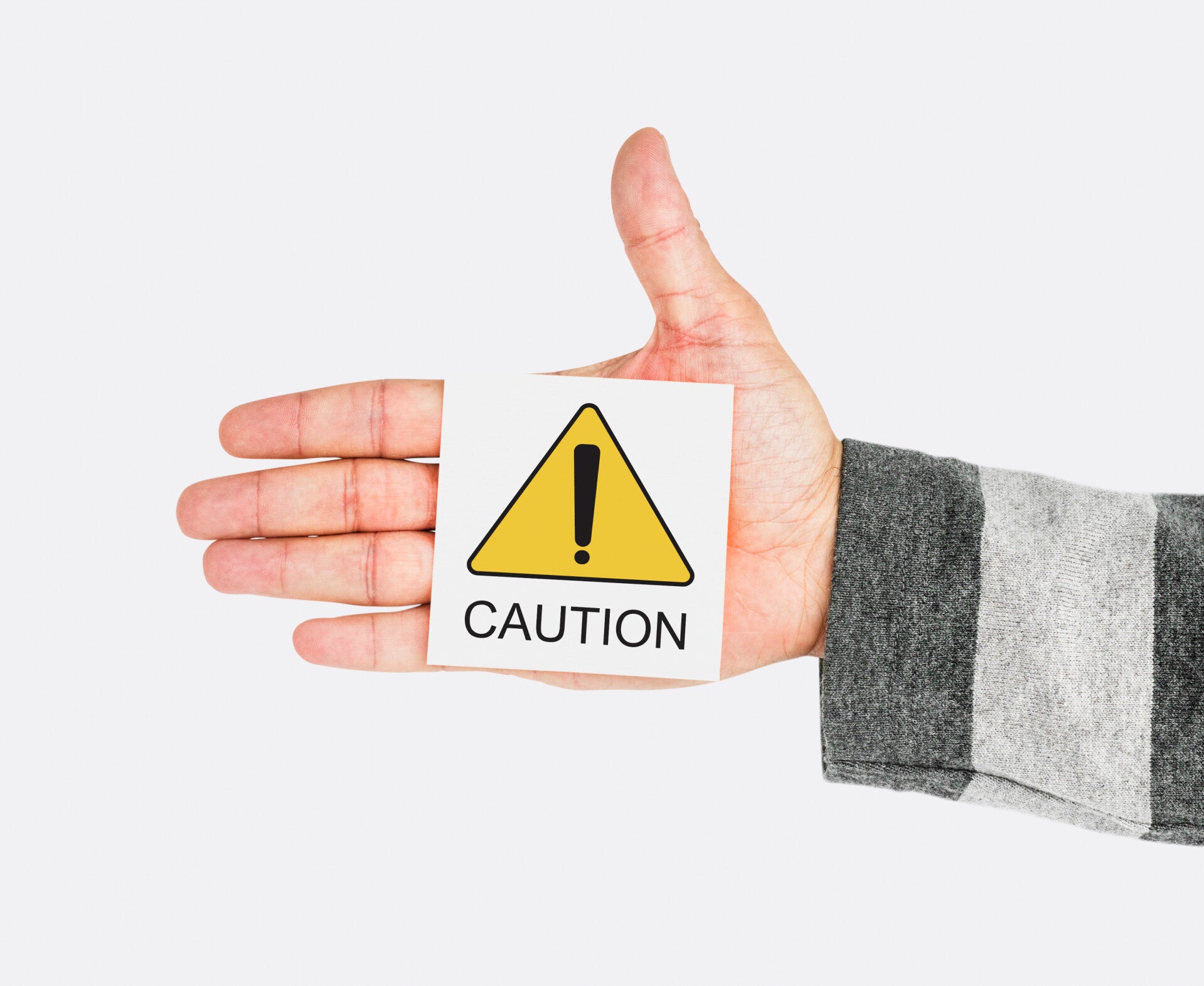 Hand eines Mannes mit Schild CAUTION - Vorsicht (englisch)