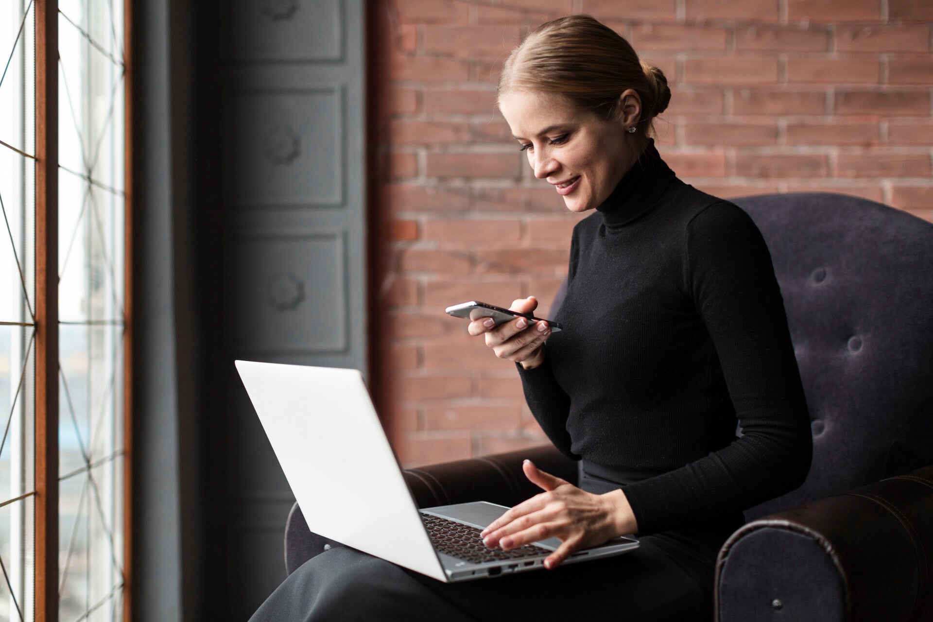 Junge Frau mit Handy in der Hand und Notebook