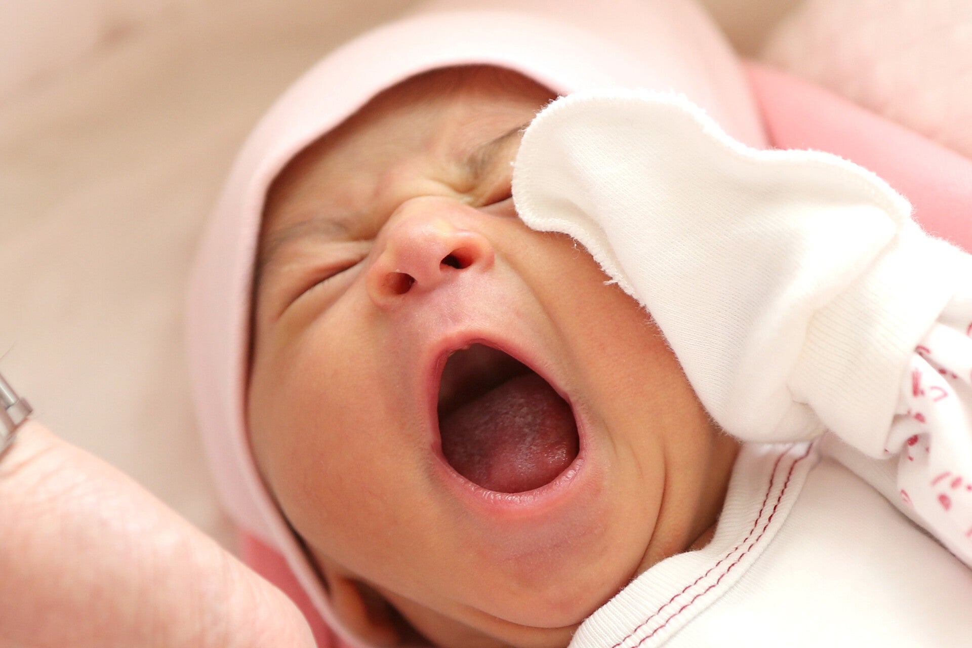 schreiendes Baby mit rosa Mützchen auf rosa Babydecke