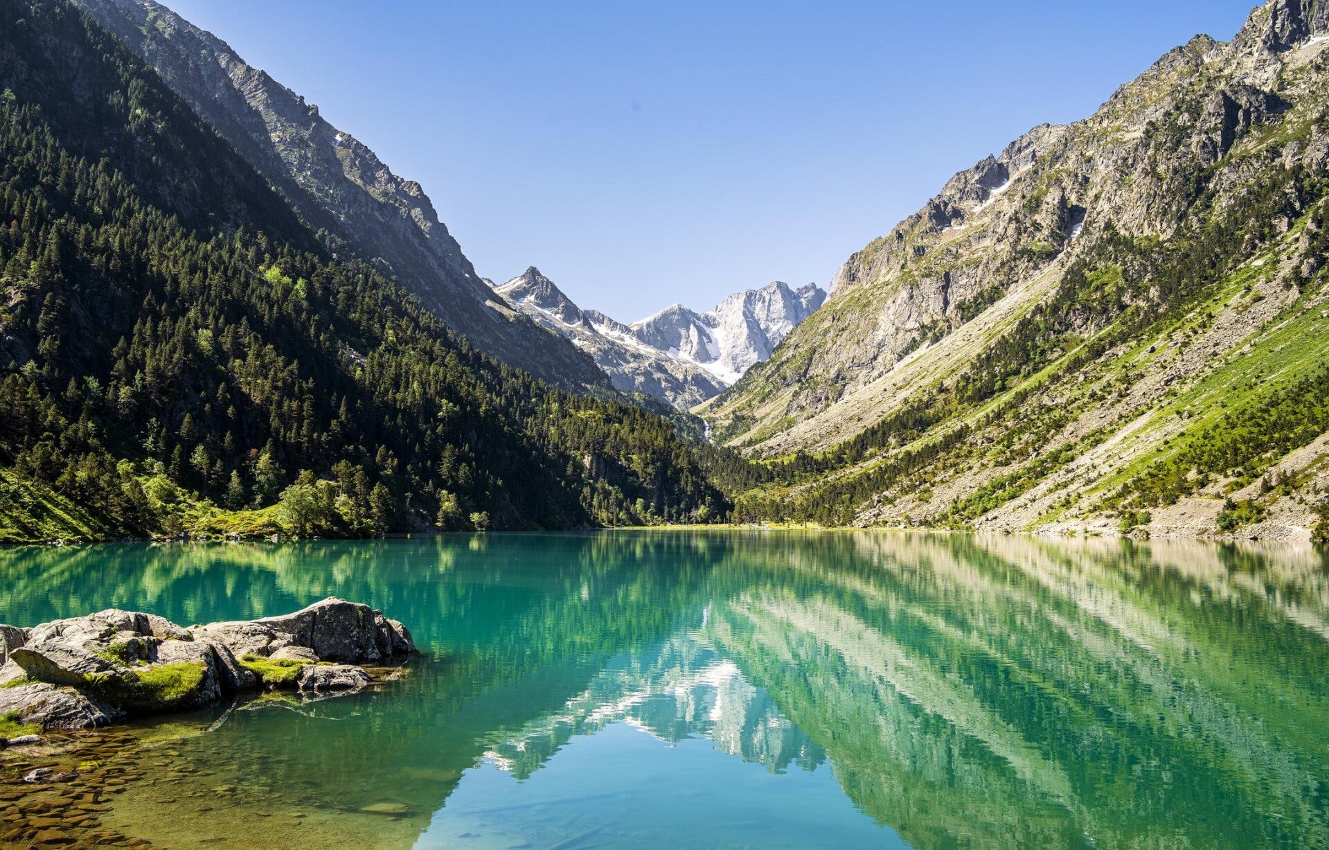 Lac de montagne turquoise entouré de sommets et de forêts dans un paysage naturel alpin.