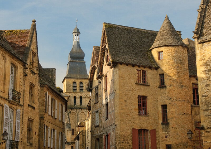 Rue du centre médiéval de Sarlat-la-Canéda en Dordogne avec maisons en pierre et clocher.