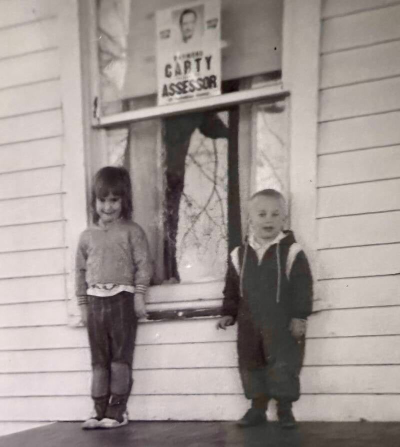 Girl and boy in front of a window with a campaign sign posted. 