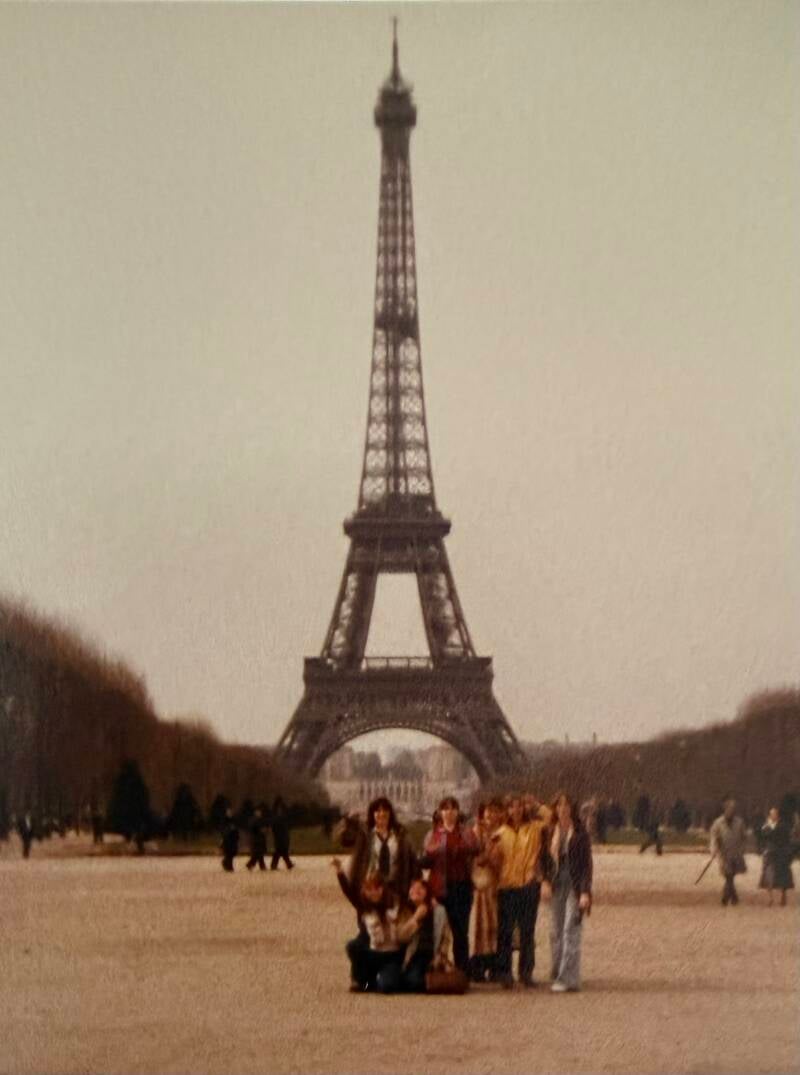 A group of high school friends posing in front of the Eiffel Tower.
