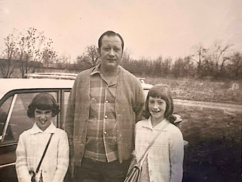Two young girls with their father dressed up in front of a car. 
