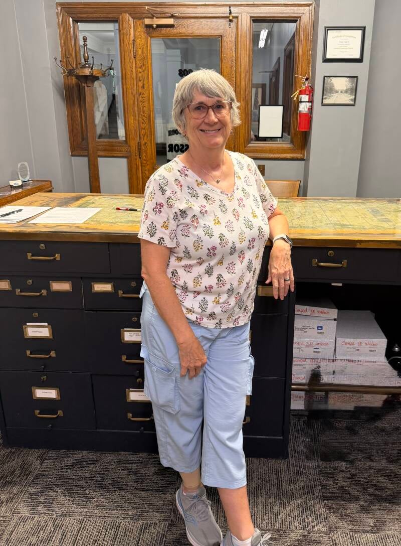 65 year old woman leaning on counter with built in file cabinets.