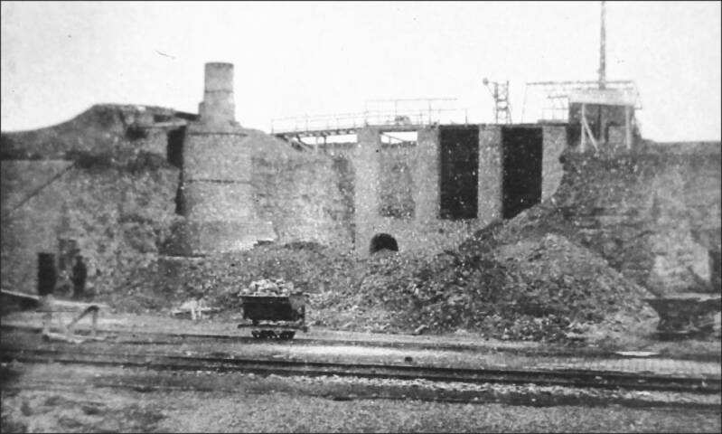afbeelding van de kalkbranderij Kroongroeven vanaf het spoor. Te zien is normaal spoor en een kipwagen op een smalspoor van de kalkbranderij. In de verte de tijdelijke veldoven en daarnaast de moderne gasoven in aanbouw.