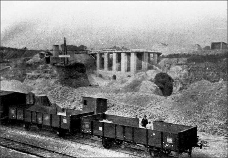 Foto genomen vanaf een van de perrons van het station van Schin op Geul die 2 open wagens en een gesloten wagen van de Staats Spoorwegen laat zien. Op de achtergrond de kalkbranderij van N.V. Vereenigde Kroongroeven.