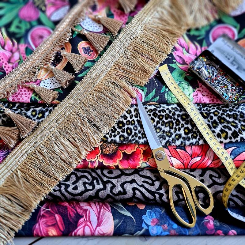 diverse stoffen met kleurrijke prints en dierenprints, naaischaar, centimeter en spelden, goudkleurig franjeband