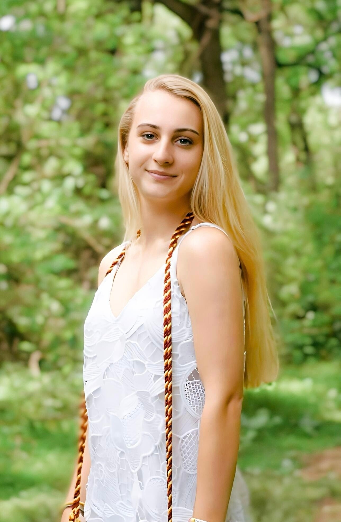 Graduation portrait of a woman outdoors in Maryland wearing a white dress with a forest background
