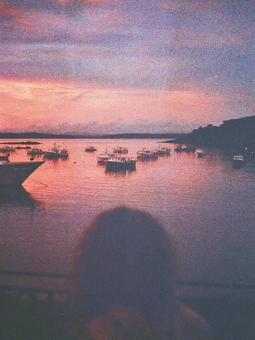 Sunset harbor scene captured on film with boats, water, and a blurred figure creating a nostalgic mood taken by Maryland film photographer.