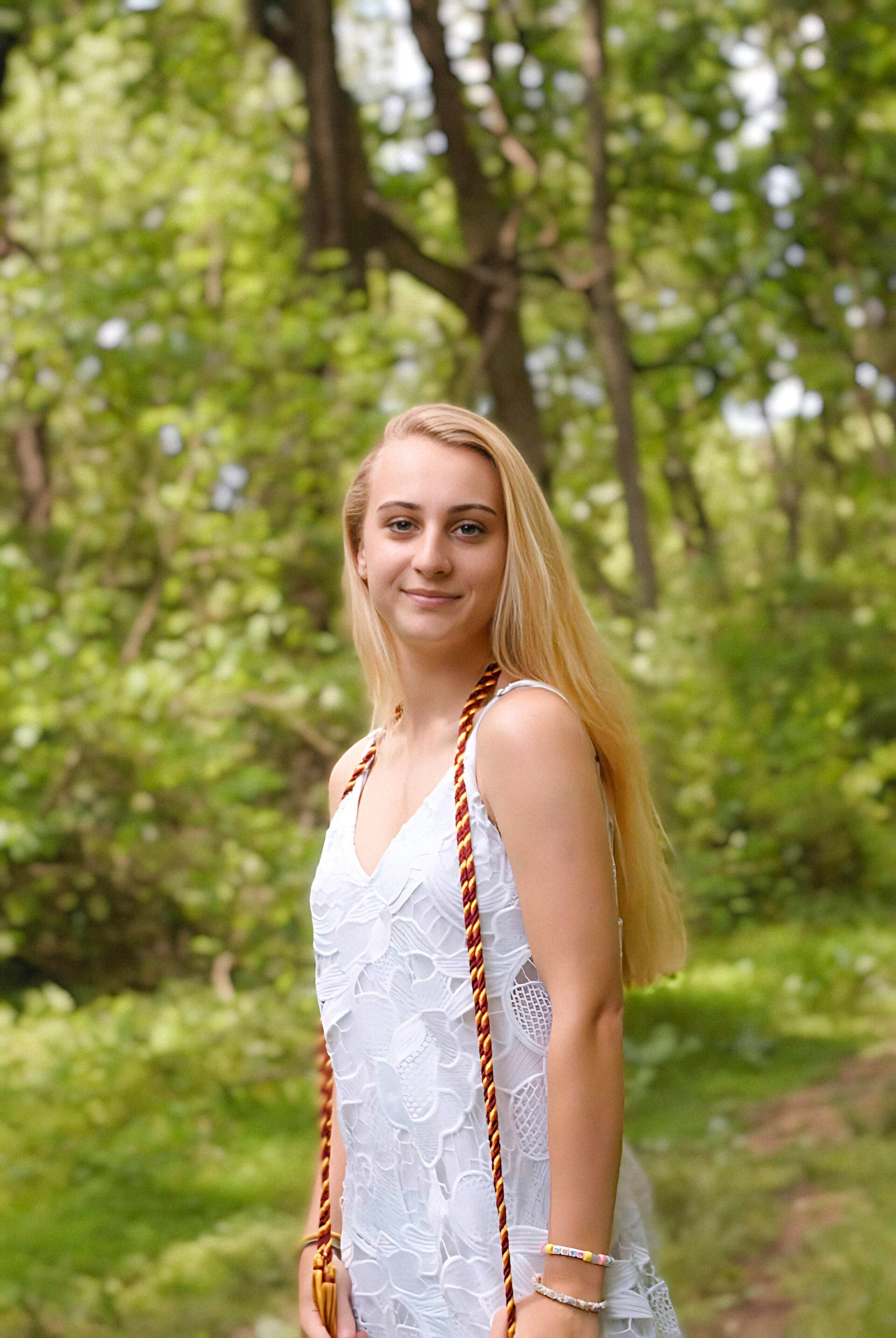 Graduation portrait of a woman outdoors in Maryland wearing a white dress with a forest background
