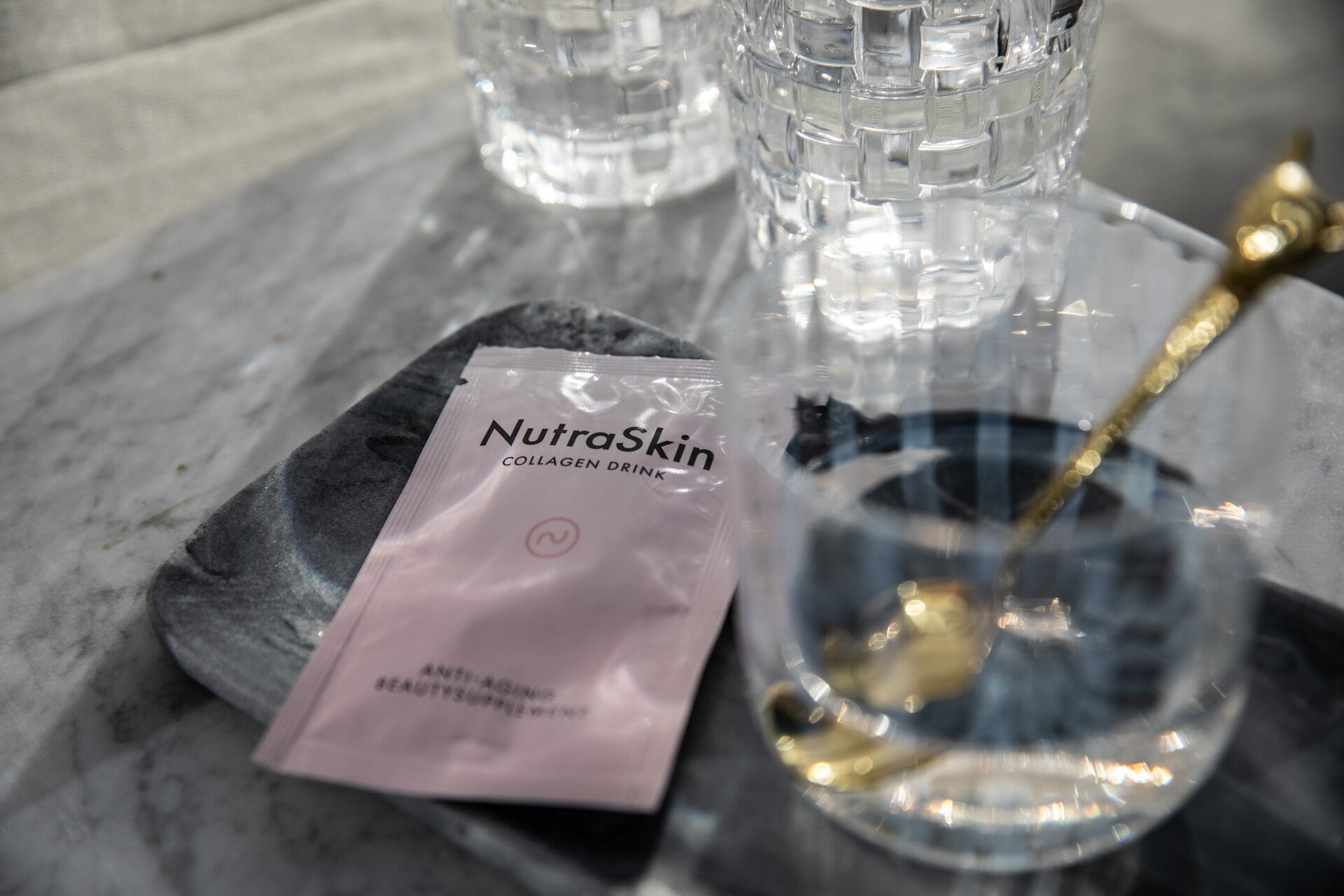 : Glas water met collageenpoeder naast een sachet, als onderdeel van een dagelijkse huidverzorging van binnenuit