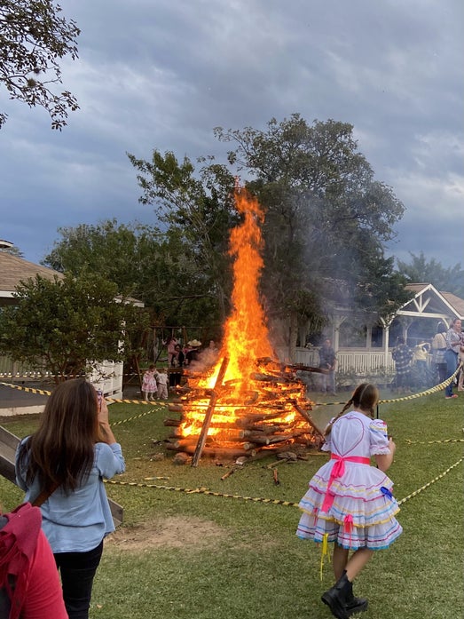 Großes Lagerfeuer mit verkleideter Frai im Vordergrund die allerdingsnur von hinten zu sehen ist.