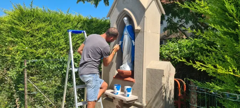 Artisan en train de restaurer et repeindre la statue de la Vierge à Saint-Bernard.