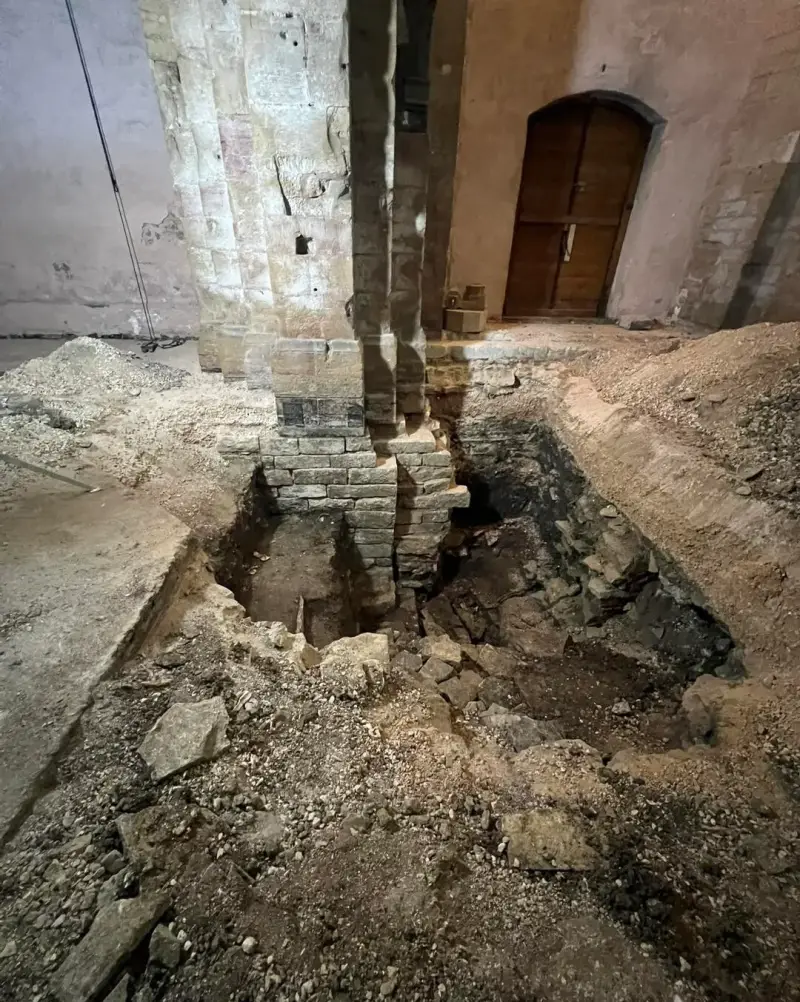 Travaux de terrassement au pied des piliers d’une église ancienne à l’aide d’une mini-pelle.