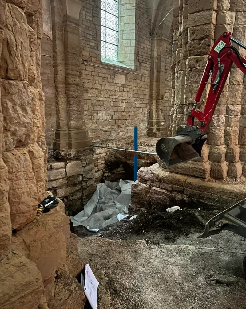 Dégagement des fondations en pierre autour d’un pilier ancien à l’intérieur d’une église.