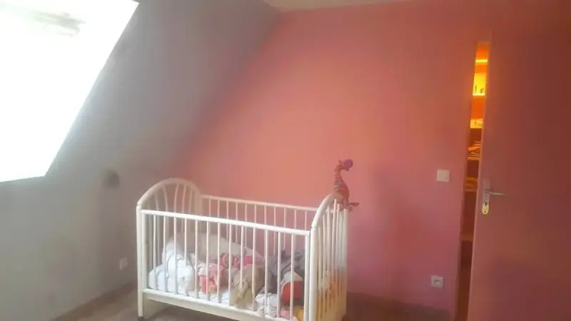 Chambre sous combles terminée à Demigny avec mur rose, parquet et lit d’enfant.