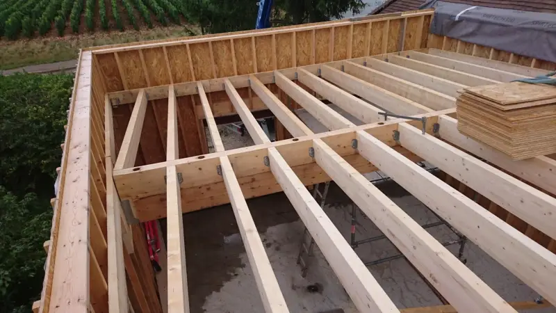 Pose du solivage en bois pour la toiture plate d’une extension de maison à Meursault.