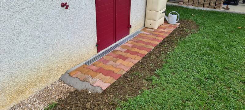 Pavage extérieur terminé à Saint-Bernard avec caniveau de drainage et allée en pavés le long de la façade.