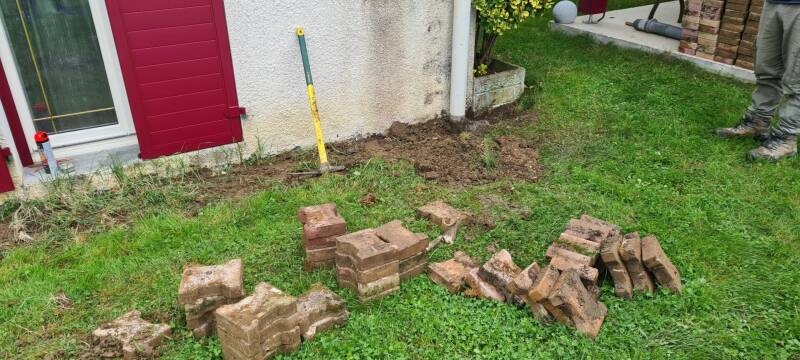Préparation d'un pavage extérieur à Saint-Bernard avec décaissement du terrain et retrait des anciens pavés le long de la maison.