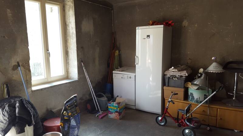 : Pièce brute avant rénovation à Corgoloin avec murs sombres, fenêtre existante et espace à repenser entièrement.