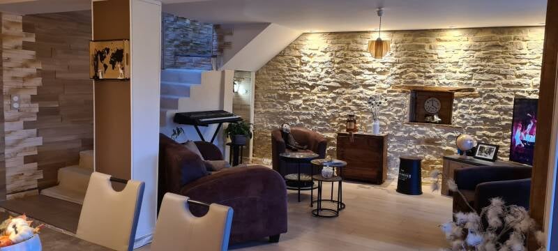 Salon rénové à Saint-Bernard avec mur en pierre et éclairage chaleureux.