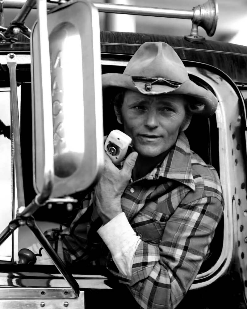 Zwart-wit portret van een klassieke vrachtwagenchauffeur met cowboyhoed en CB-radio in de cabine van zijn truck. De foto ademt oldschool trucker culture, vrijheid, vakmanschap en het onvervalste leven op de weg. Een sterk beeld voor liefhebbers van klassi