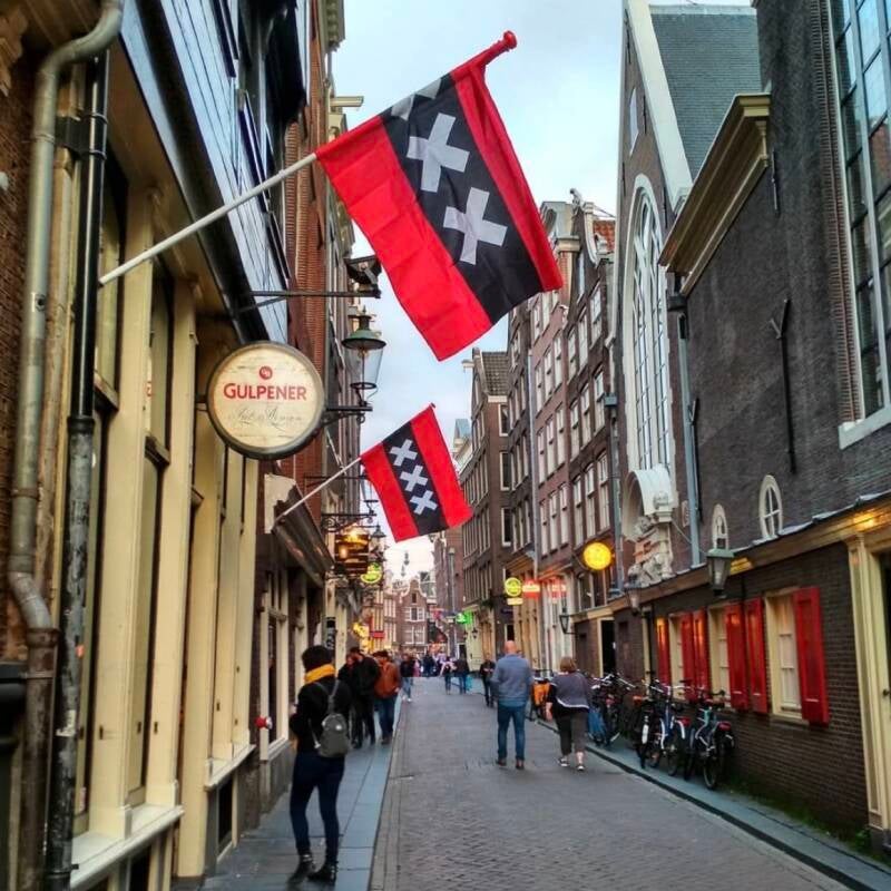 A serene Amsterdam street scene featuring historic flags with the three red crosses, symbolizing civic pride.