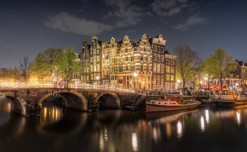 A serene Amsterdam canal at night, with glowing lights reflecting on the calm water, creating a magical atmosphere.
