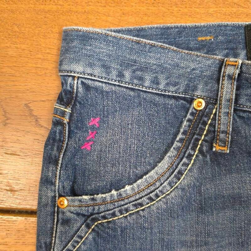 Close-up of embroidered belt loops with three pink crosses – Hand-stitched pink crosses on denim belt loops, inspired by Amsterdam’s coat of arms.