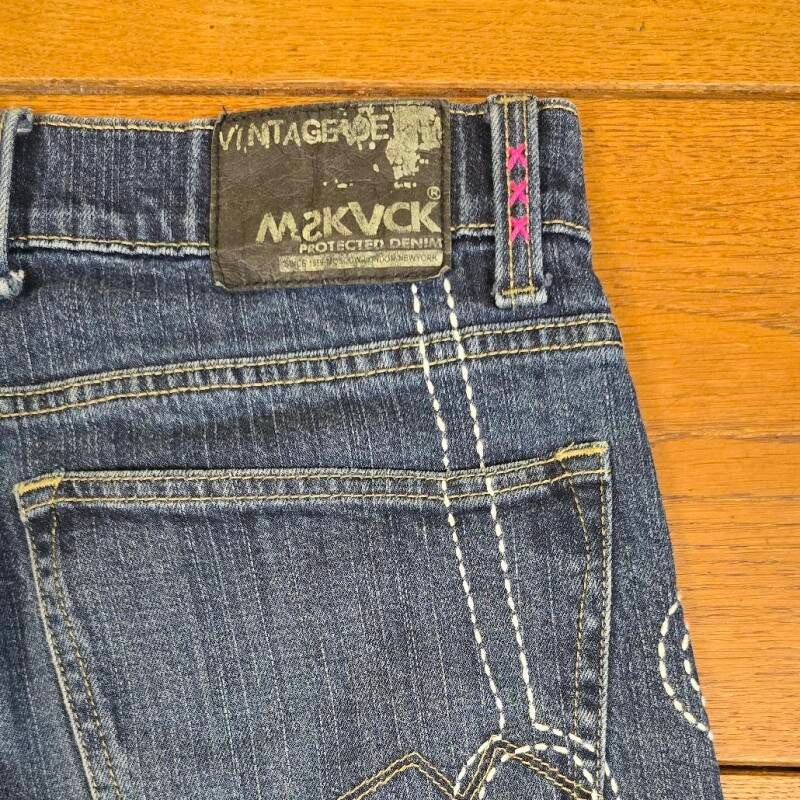 Close-up of embroidered belt loops with three pink crosses – Hand-stitched pink crosses on denim belt loops, inspired by Amsterdam’s coat of arms.