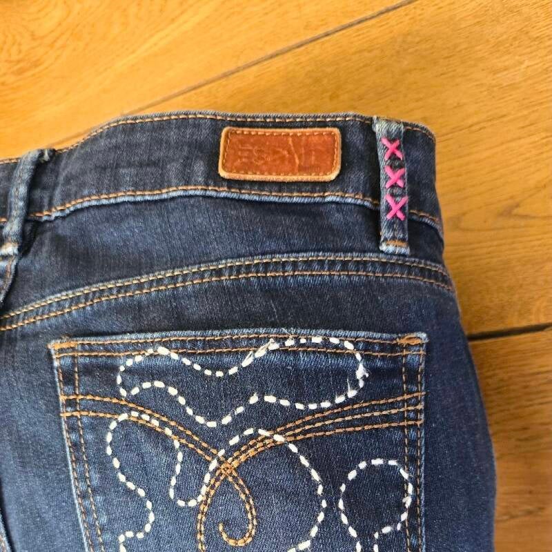 Close-up of embroidered belt loops with three pink crosses – Hand-stitched pink crosses on denim belt loops, inspired by Amsterdam’s coat of arms.