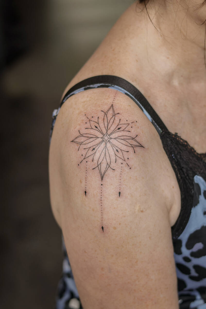 Filigranes Fineline-Tattoo eines floralen Sterns auf dem Oberarm.