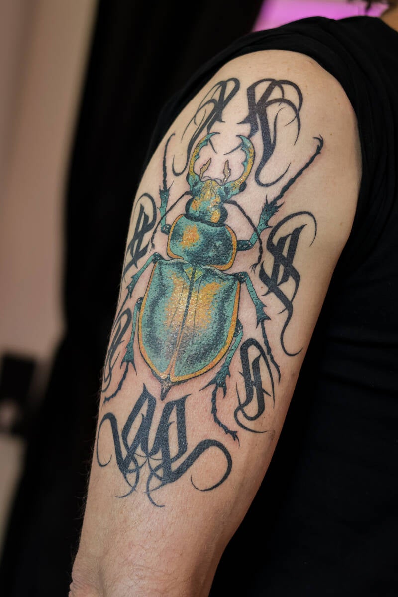 Farbiges Hirschkäfer-Tattoo mit schwarzem Gothic-Lettering.