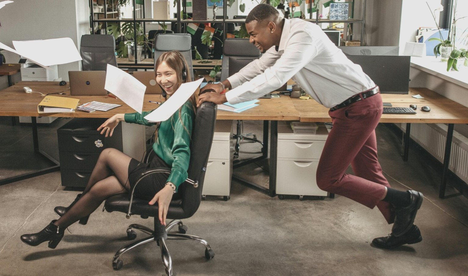 kantoorsetting met twee mensen die plezier maken. De man duwt de vrouw op een bureaustoel door de ruimte en ze lachen.
