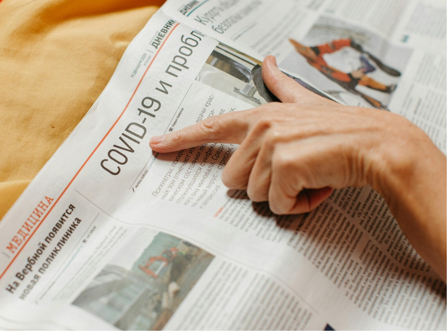 Een open geslagen krant met een artikel over COVID 19, waar iemand met de vinger naar de titel wijst