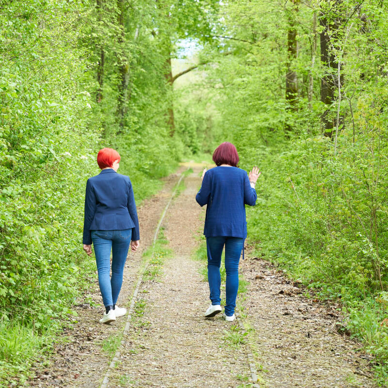 Stephanie Breschniak hört während einem Gang in der Natur zu. Es ist die Skoliose von Frau Breschniak gut sichtbar durch die Kleidung.